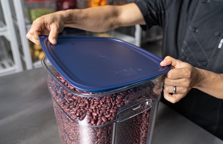 Closeup of a persons hands opening a Cambro CamSquare container filled with beans.