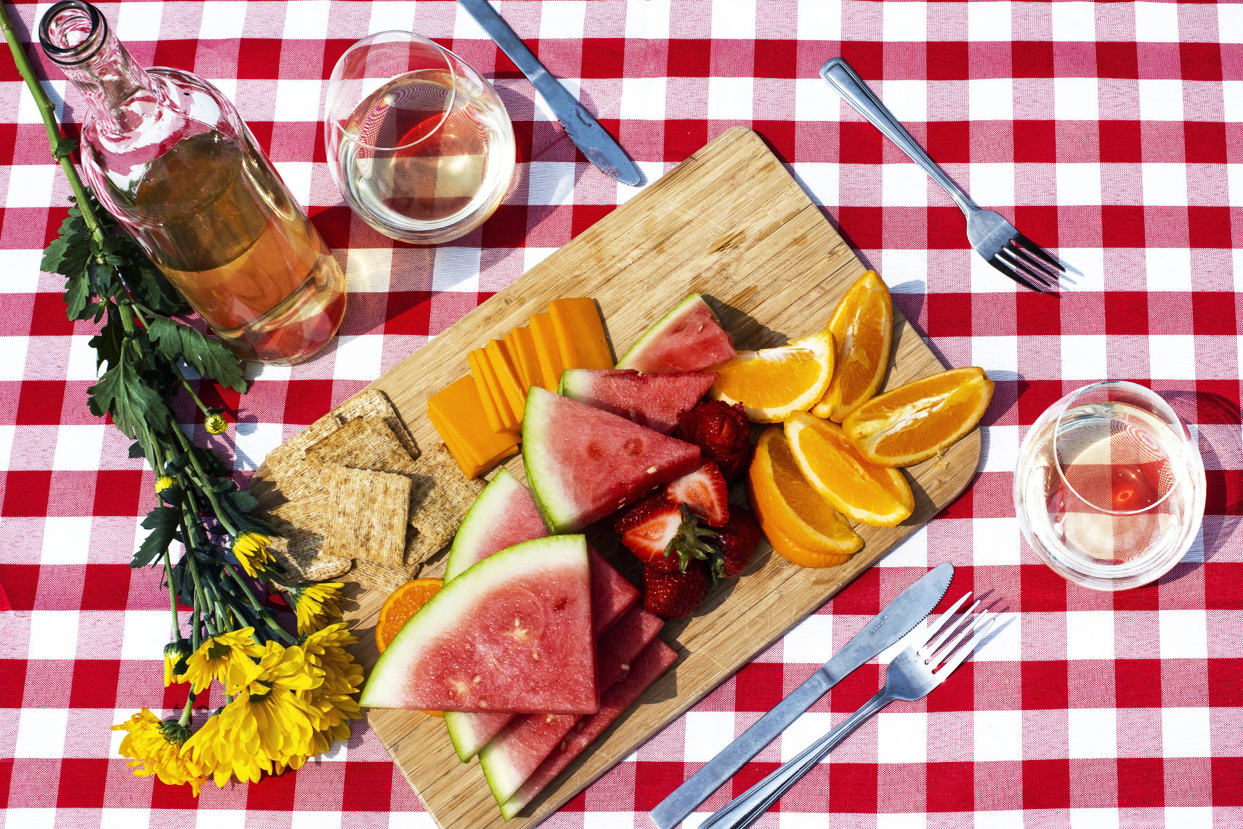 Overhead shot of cutting board with fruits, cheese and crackers on picnic blanket