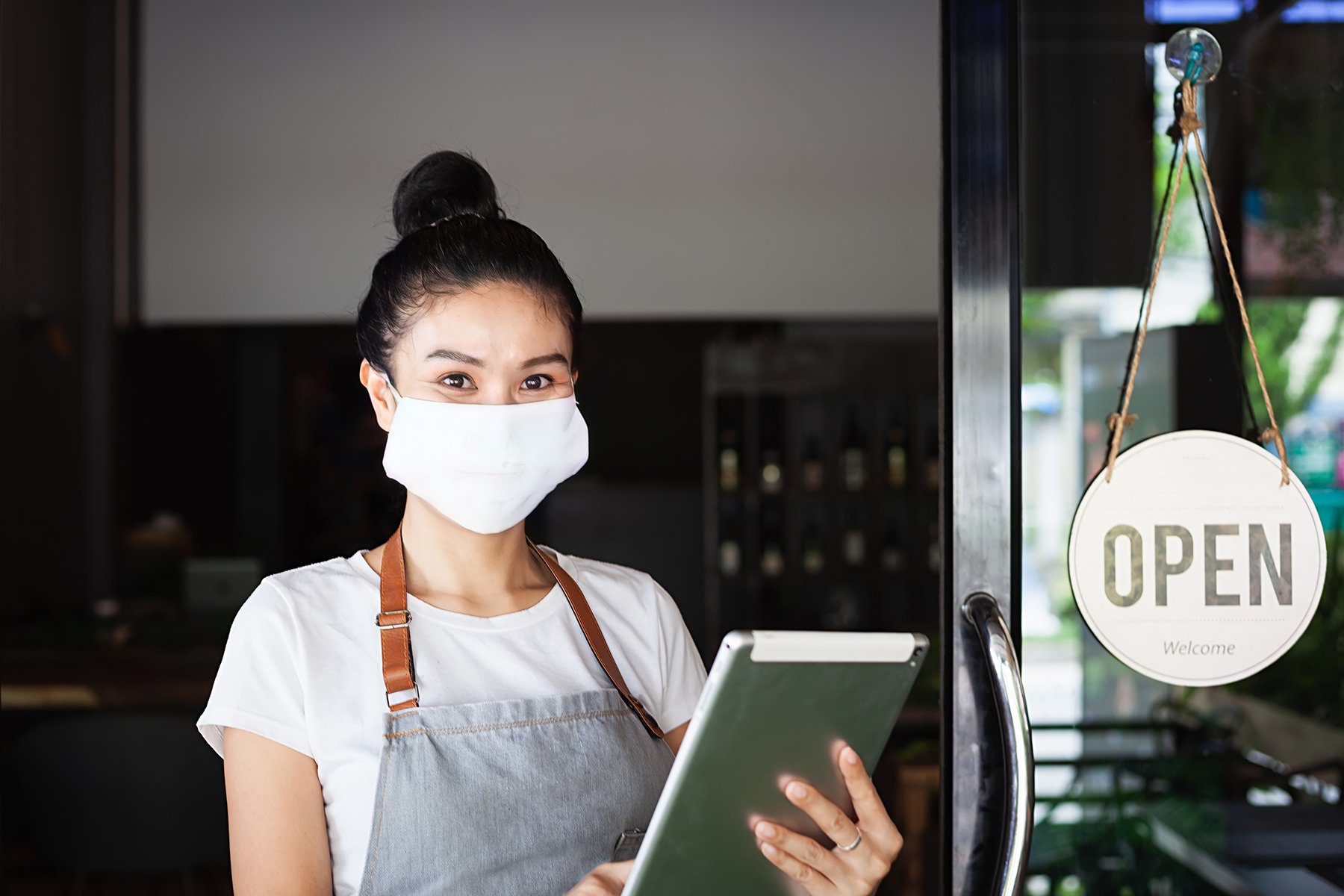 Restaurant worker with clipboard ready for orders, standing next to hanging OPEN sign