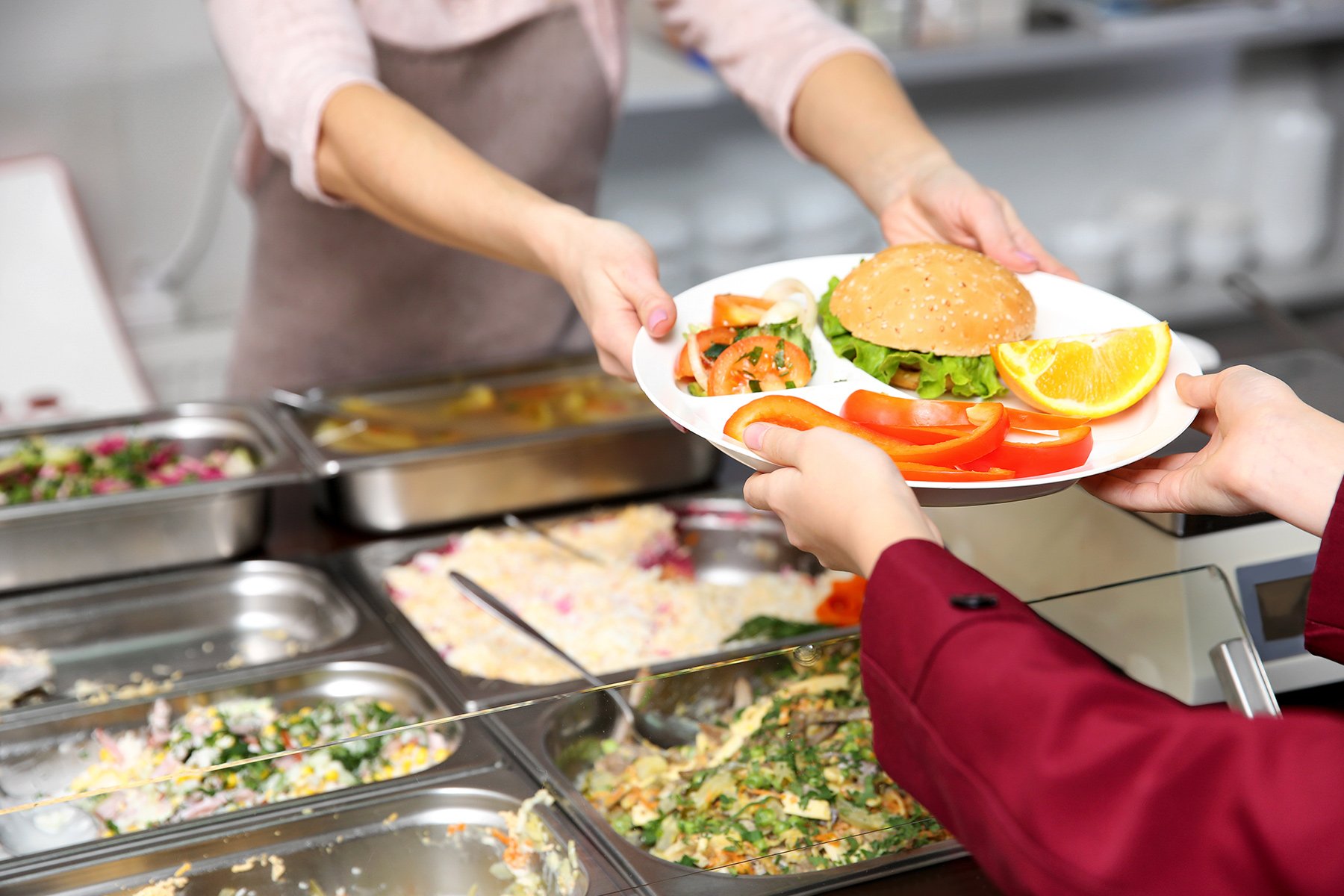 Cafeteria worker handing out plate of food to diner