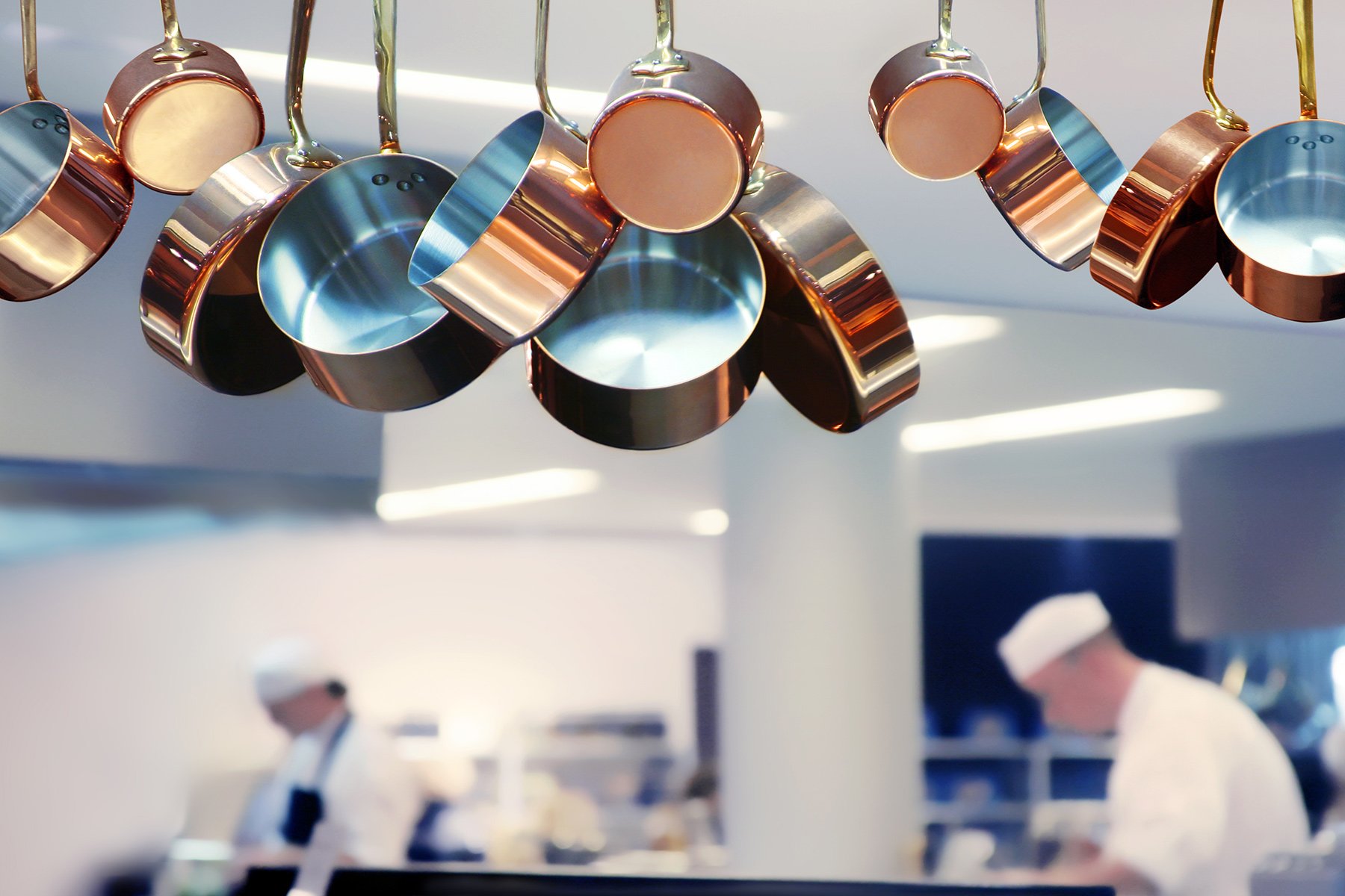 Stainless Steel pots hanging in restaurant kitchen with bokeh background