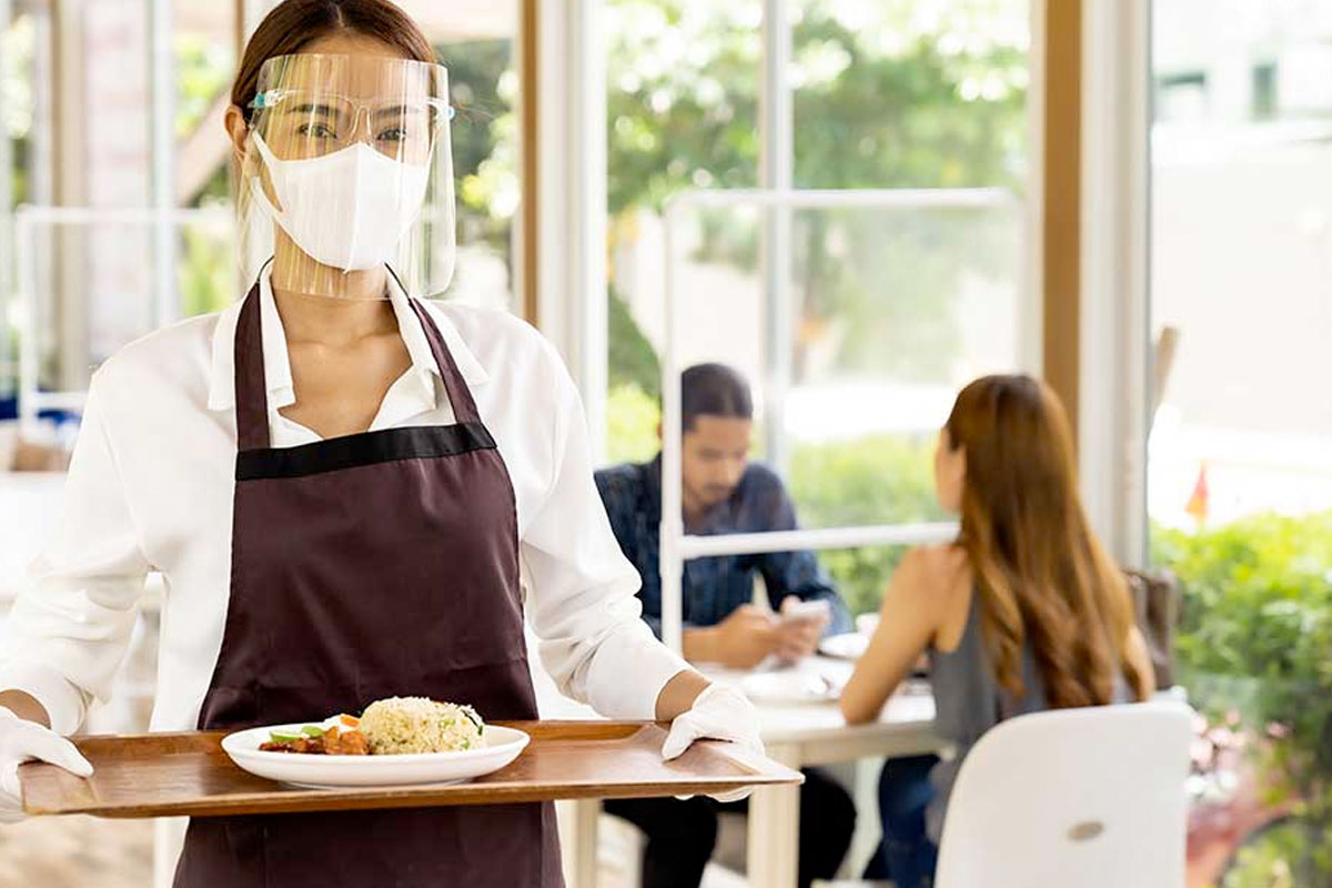 waitress wearing face shield to serve a meal to customers