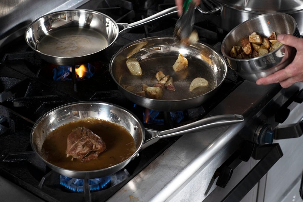 chef putting potatoes into a heated pan with two additional pans on the stove in view