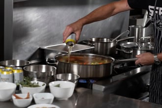 chef pouring liquid into a pan full of vegetables