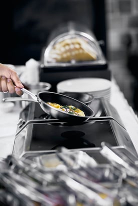chef's hand raising pan from induction stove to flip the food