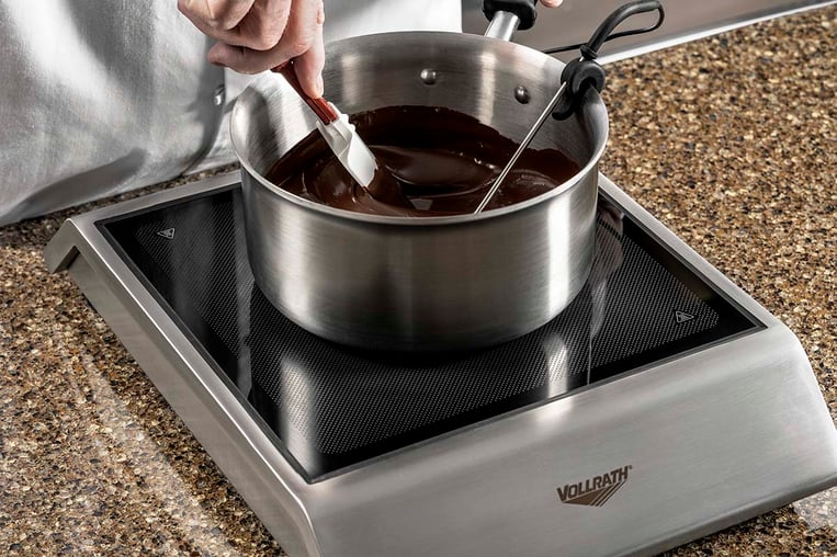 chef melting chocolate in a pot over an induction stove