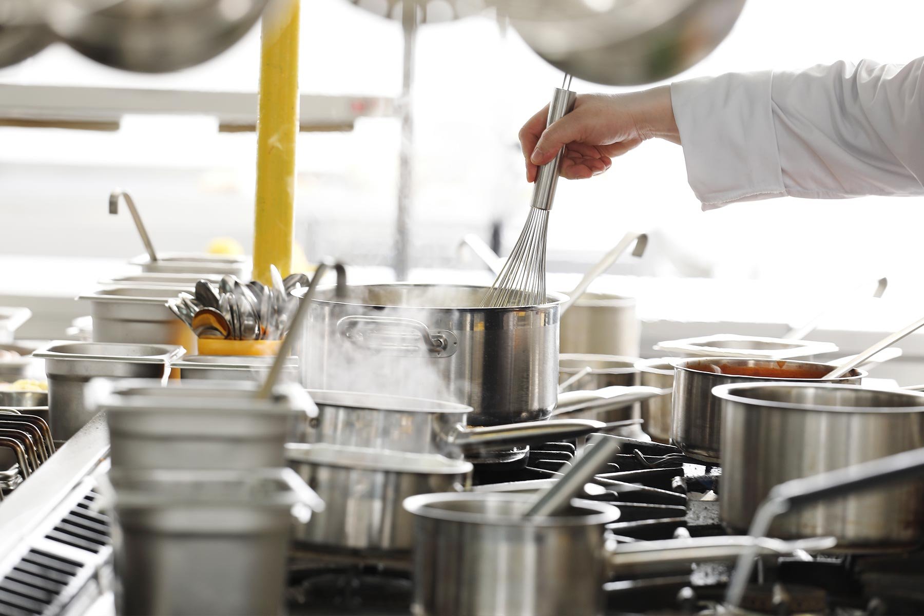 Chef whisking food in pot with other pots surrounding