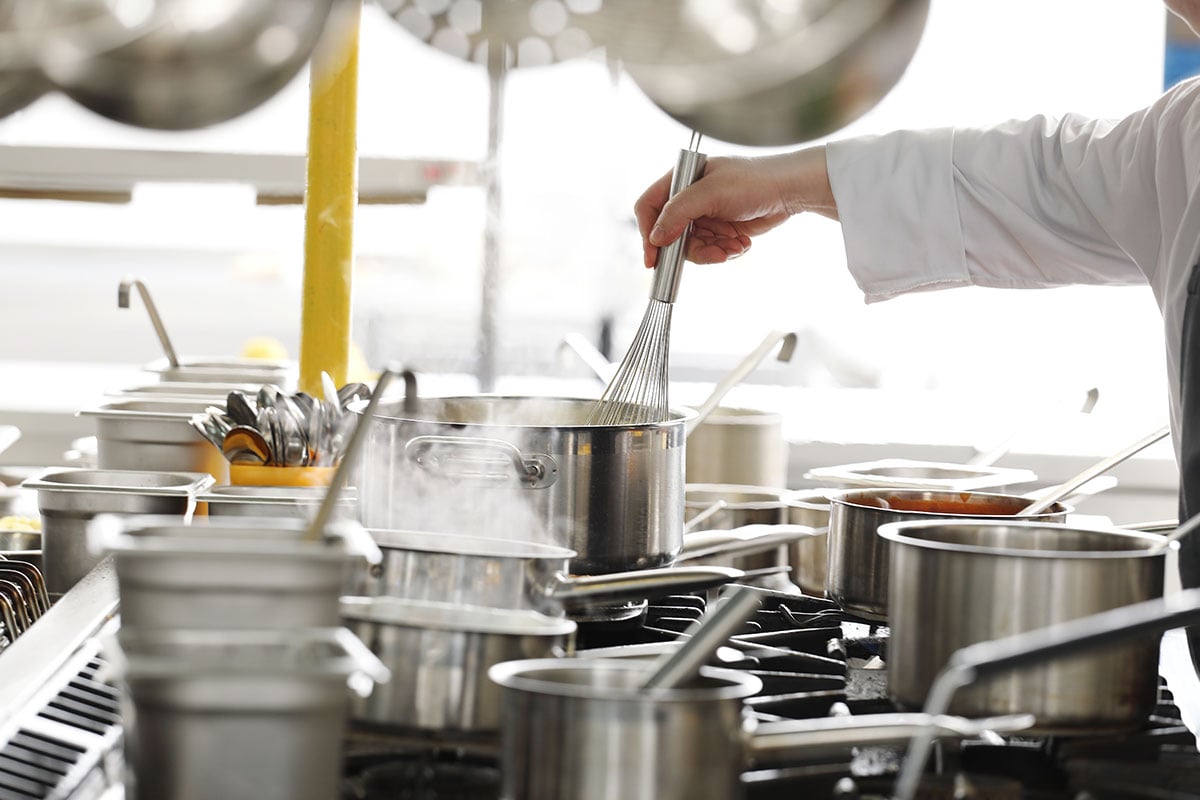 Chef whisking food in pot with multiple other pots on the stove
