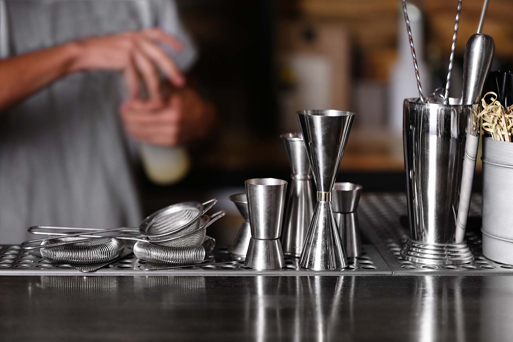 Bar equipment on counter with a bartender mixing a drink in the background