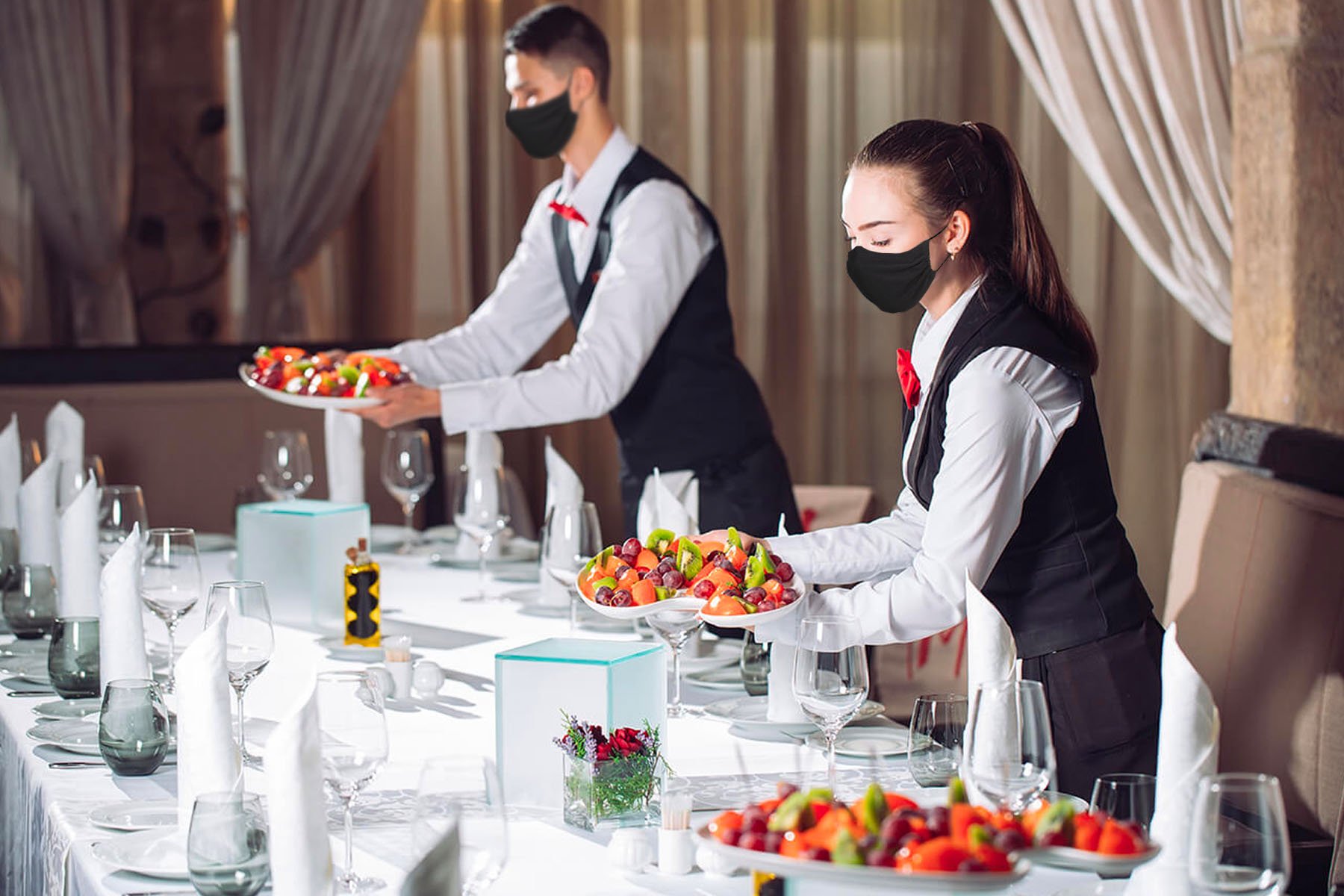 Male and female servers wearing black masks setting fruit plates down on a set table