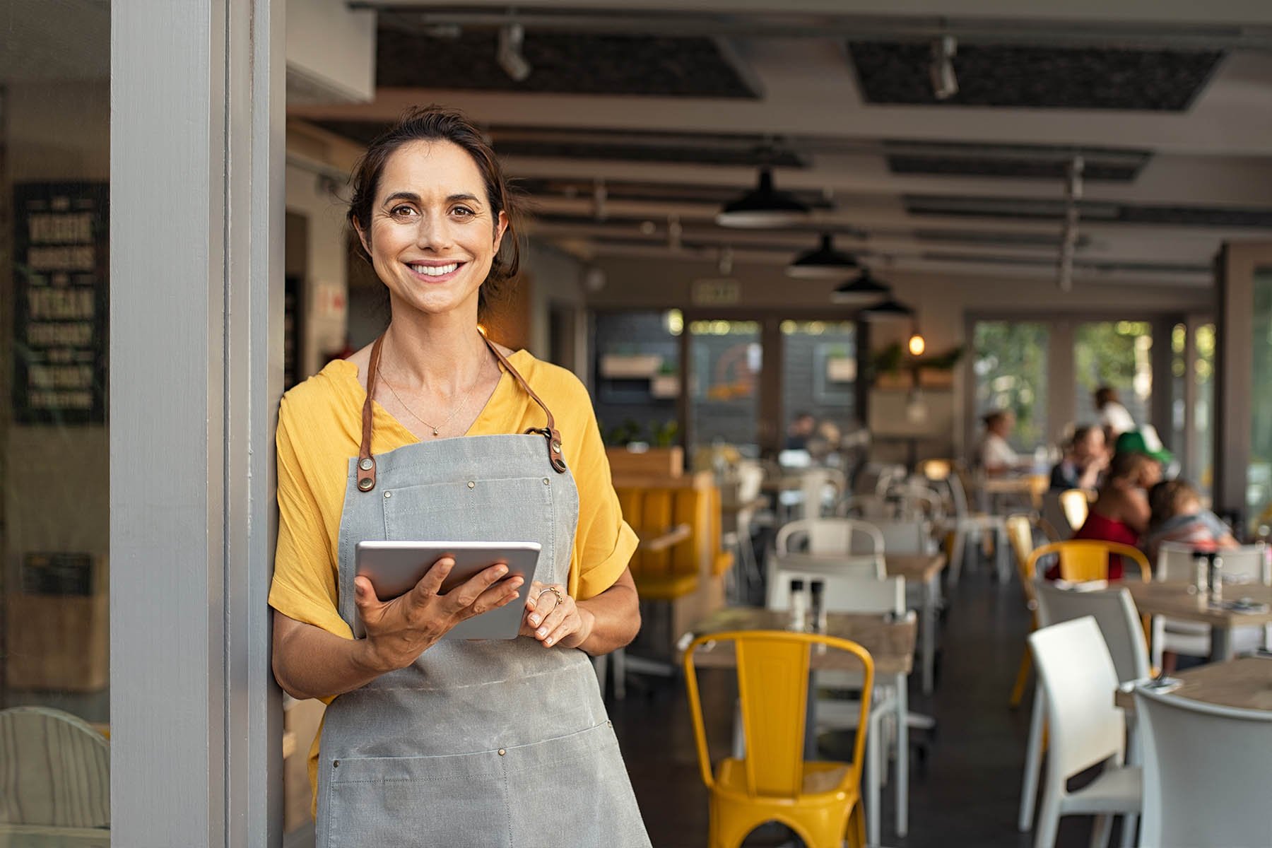 restaurant owner smiling at the camera in front of the restaurant holding a tablet in her hand