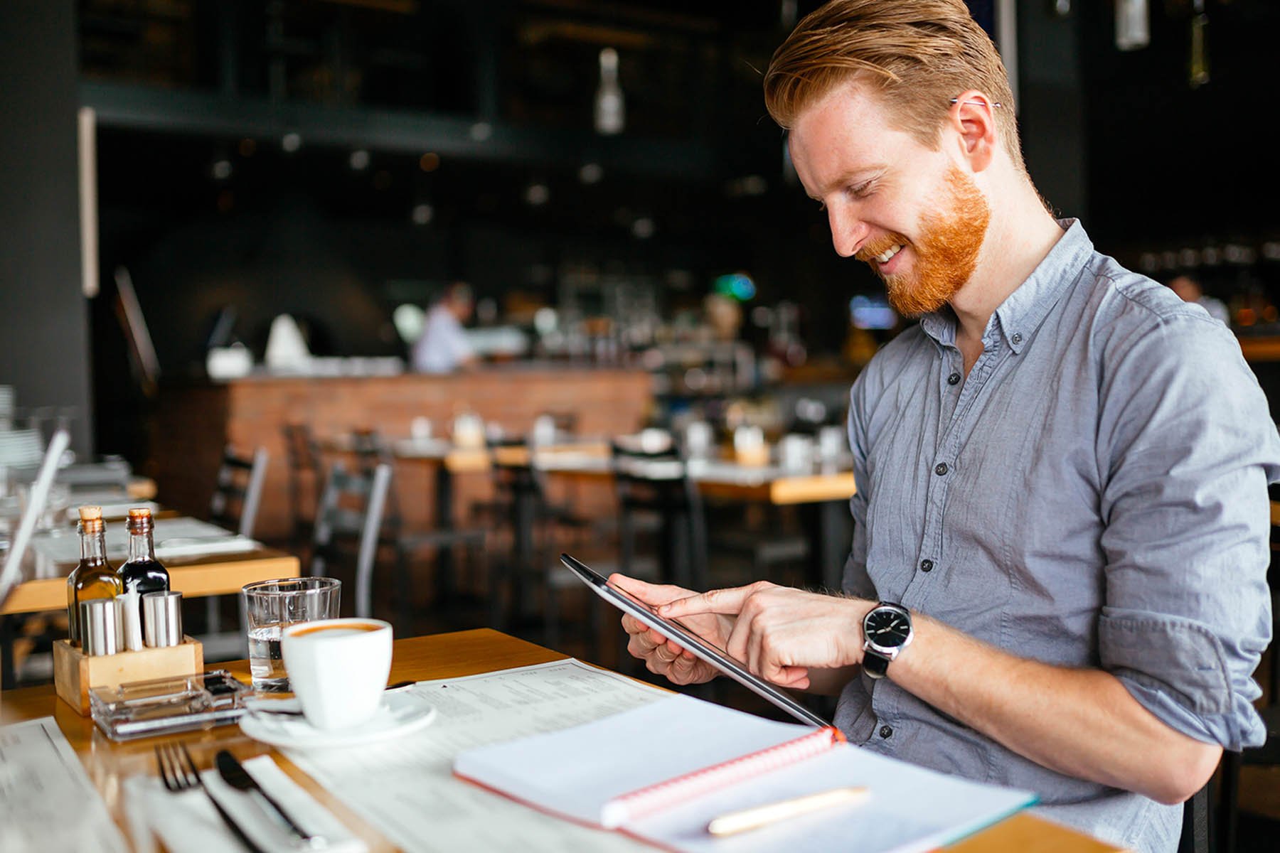 Restaurant owner reviewing information on tablet while sitting at a table at his restuarant