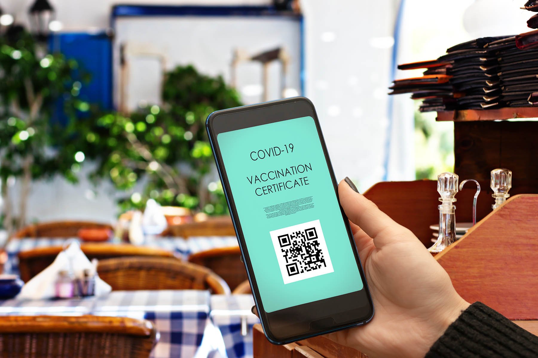 woman's hand holding a cellphone with a vaccine certificate on the screen inside of a restaurant
