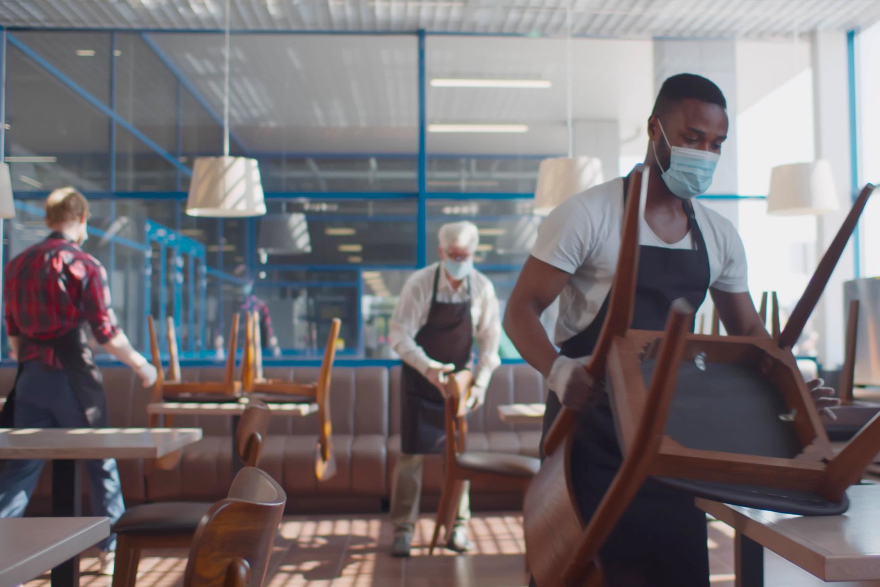 Restaurant workers with covid masks closing up restaurant and stacking chairs