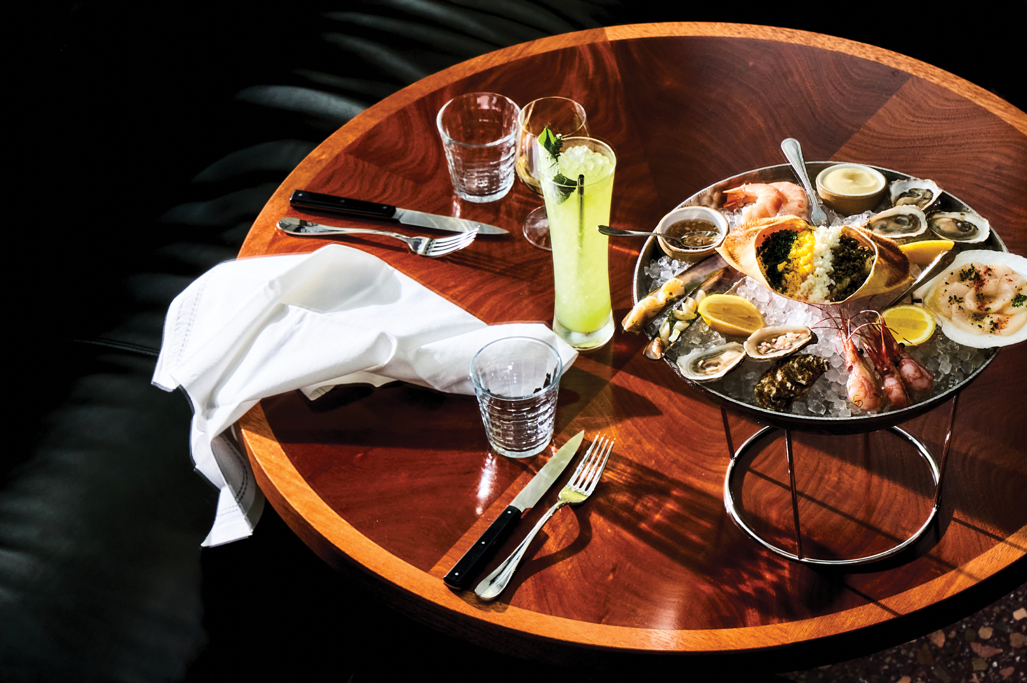 A seafood platter on ice on a wooden table with glasses and cutlery.