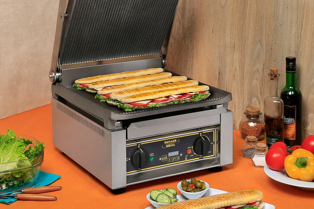Sandwiches on a panini grill with other food items on the table around it.