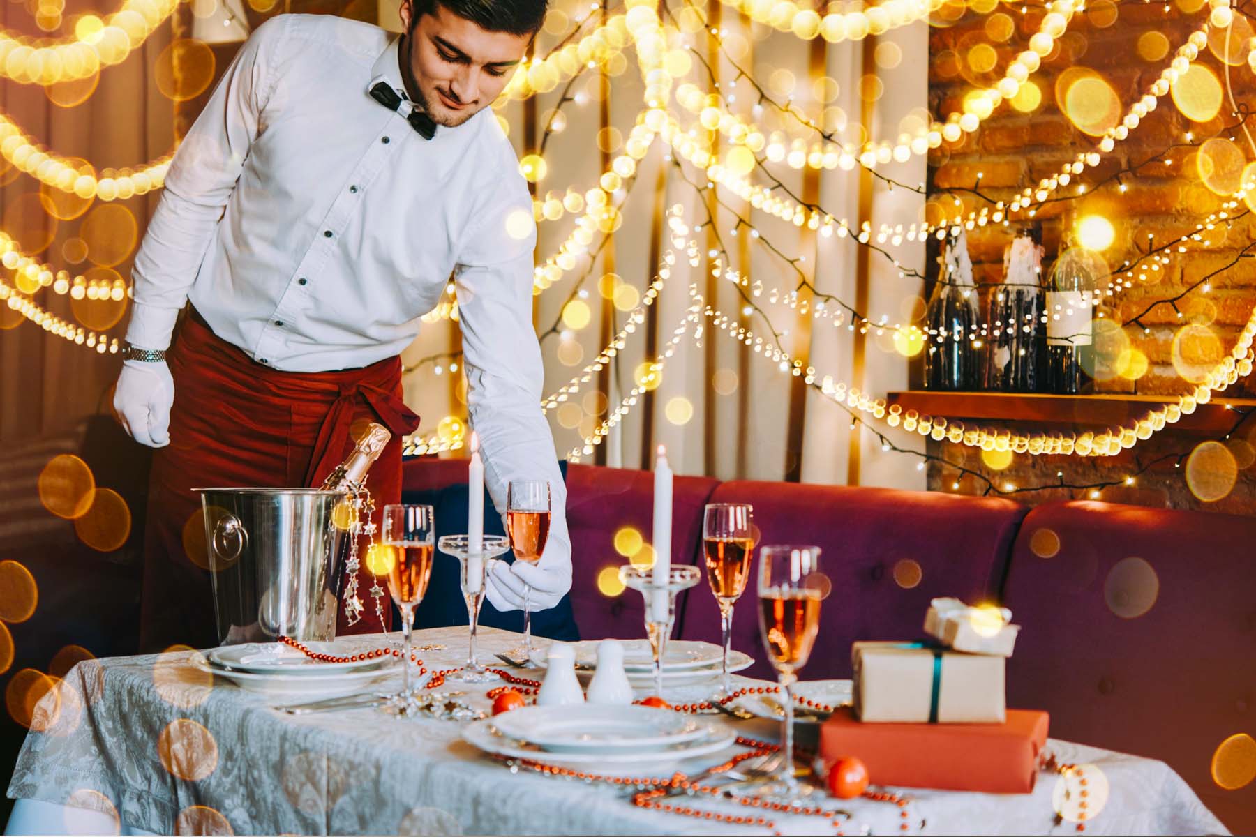 waiter setting filled champagne glasses on the table at a restaurant decorated for the holiday season