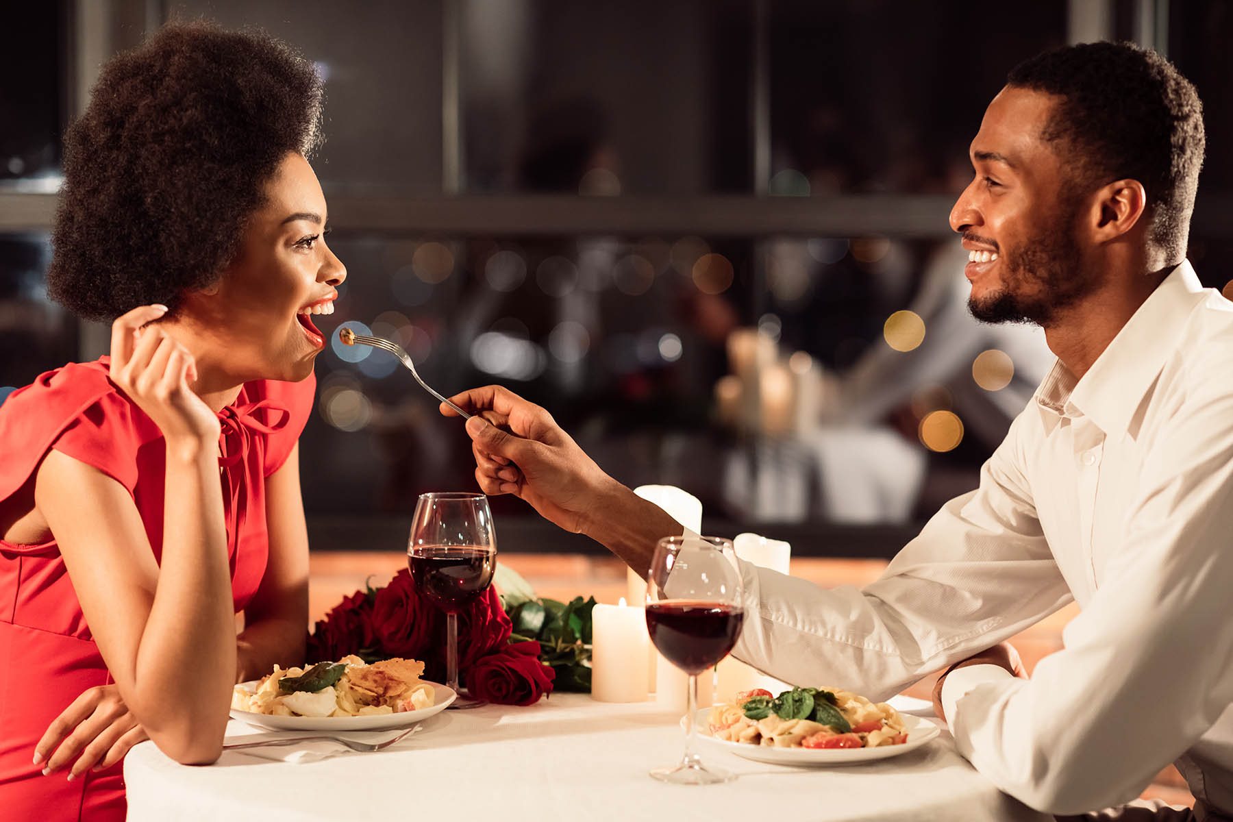 couple having a romantic dinner at a restaurant with the man holding a fork of food for his girlfriend to try