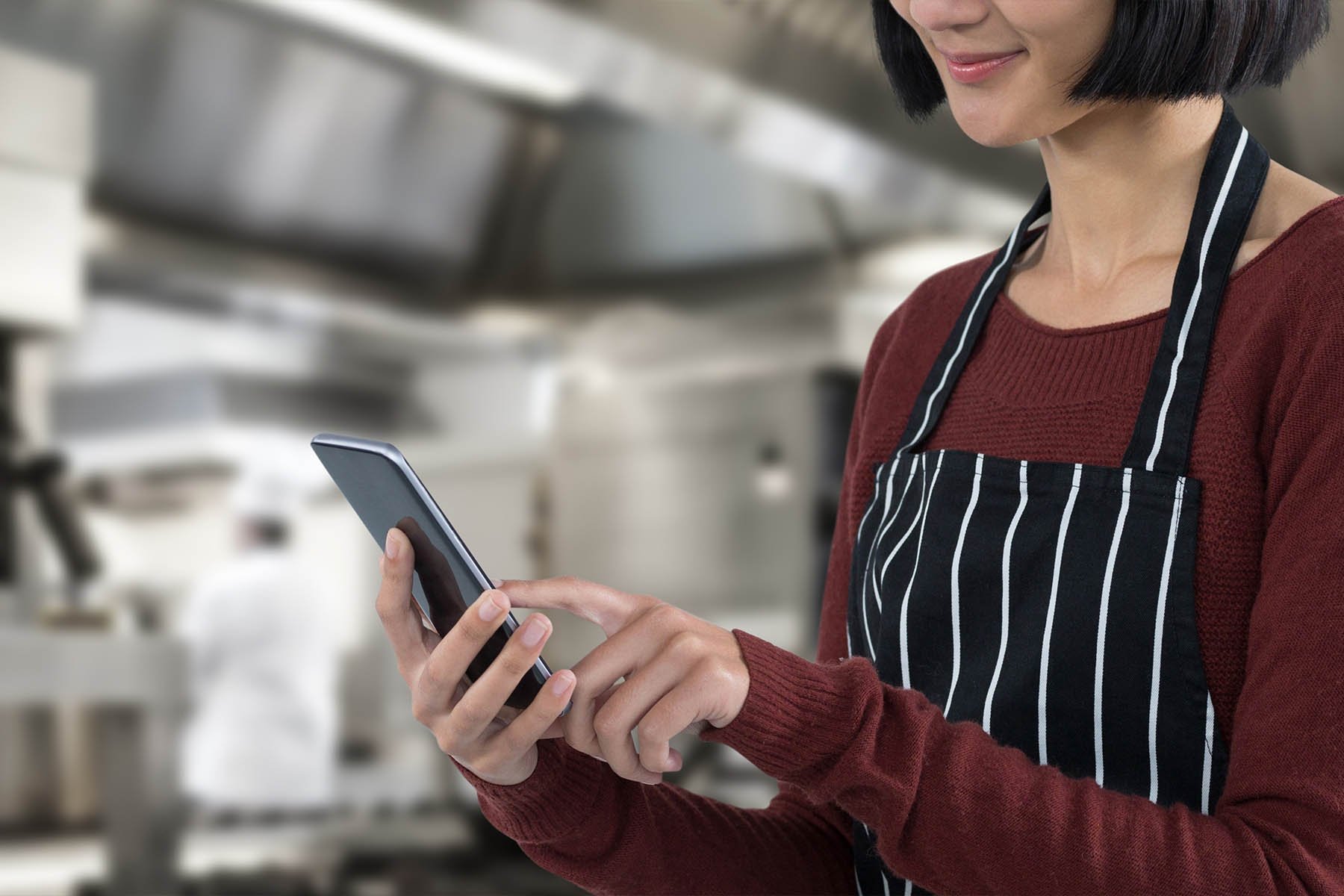 waitress in an apron typing on her cell phone with a restaurant kitchen background